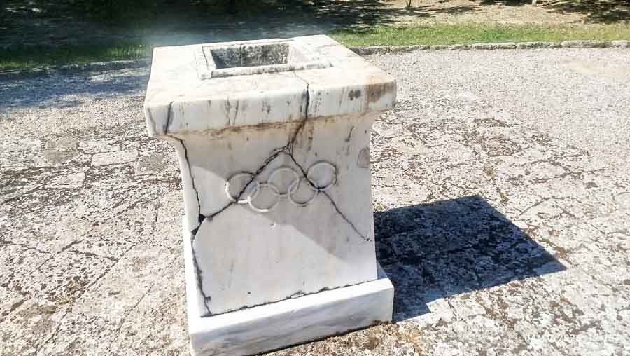 Ancient Olympia Αρχαία Ολυμπία: Εκεί όπου γεννήθηκε το Ολυμπιακό ιδεώδες 2 Μαρμάρινη βάση με ανάγλυφους τους Ολυμπιακούς Κύκλους στον αρχαιολογικό χώρο της Αρχαίας Ολυμπίας.